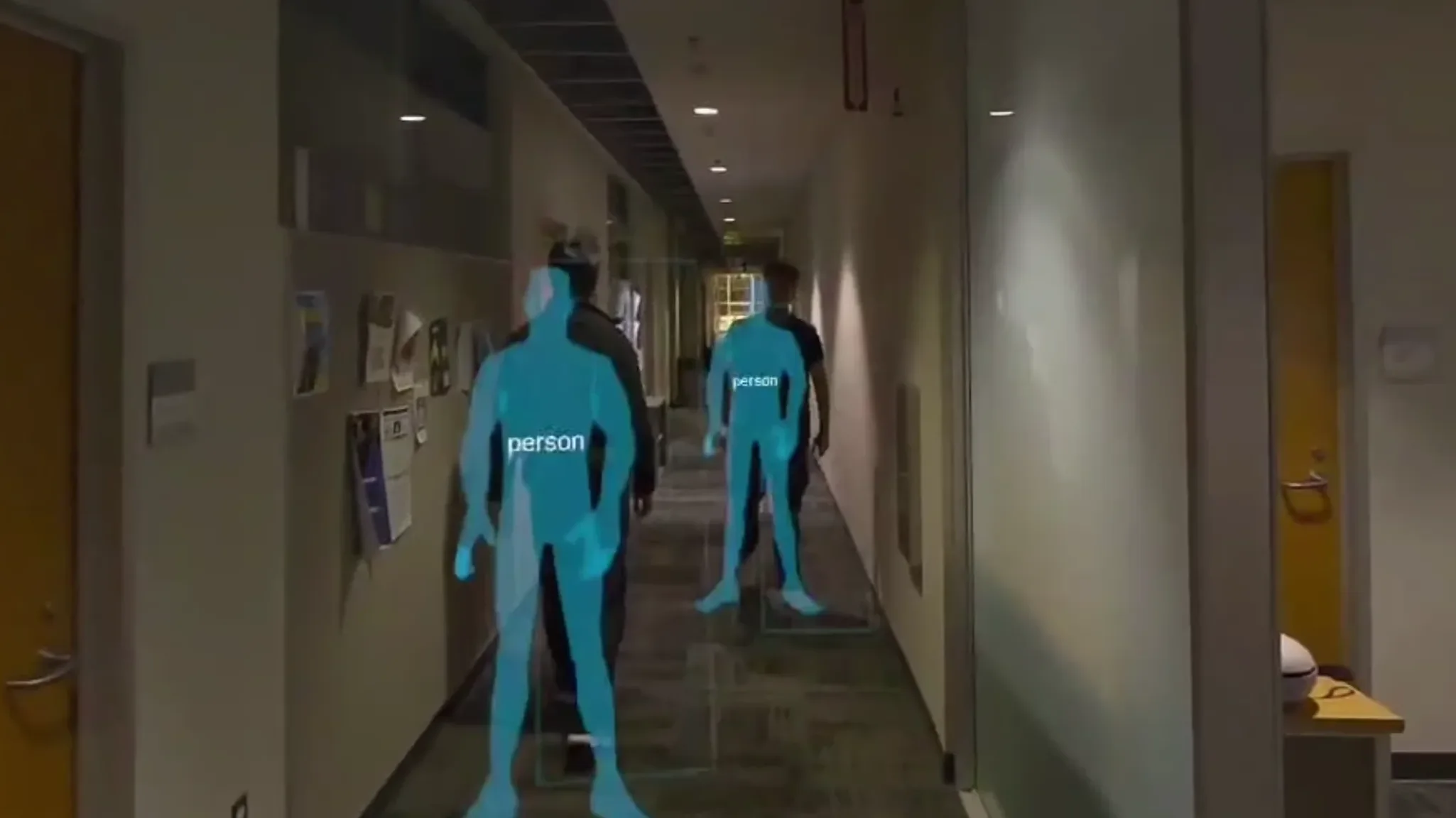 Quest 3 passthrough capture of an office hallway: two people overlaid with translucent blue silhouettes tagged “person”.
